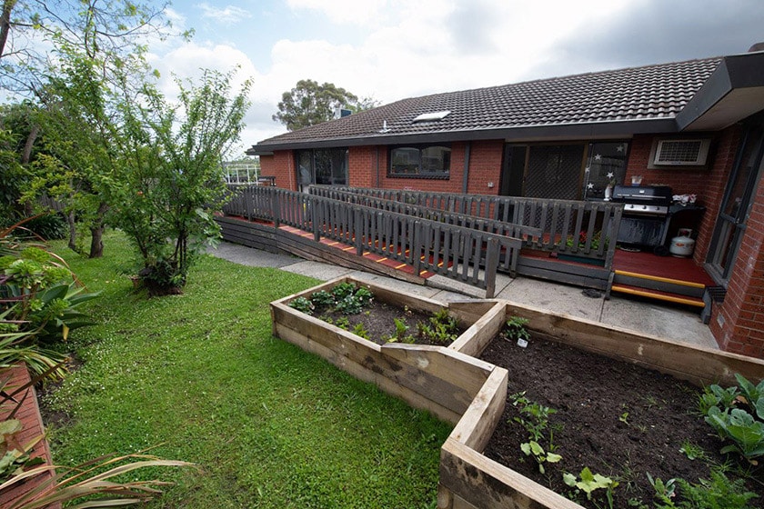 A large ramp leads down from the house to the backyard with a garden bed and lawn.