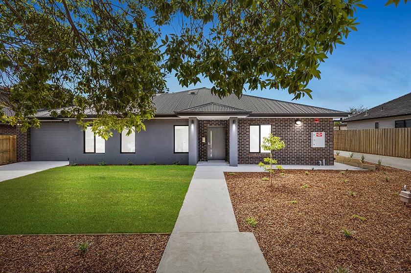 A large, modern house with a tree and lawn out the front.