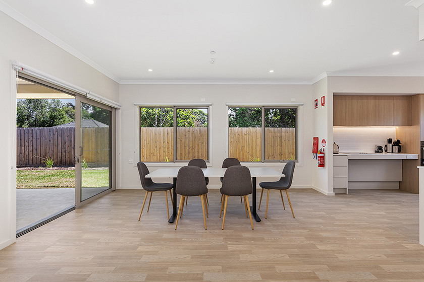 A big, modern entertaining area showing a dining table surrounded by large windows that lead into a backyard.