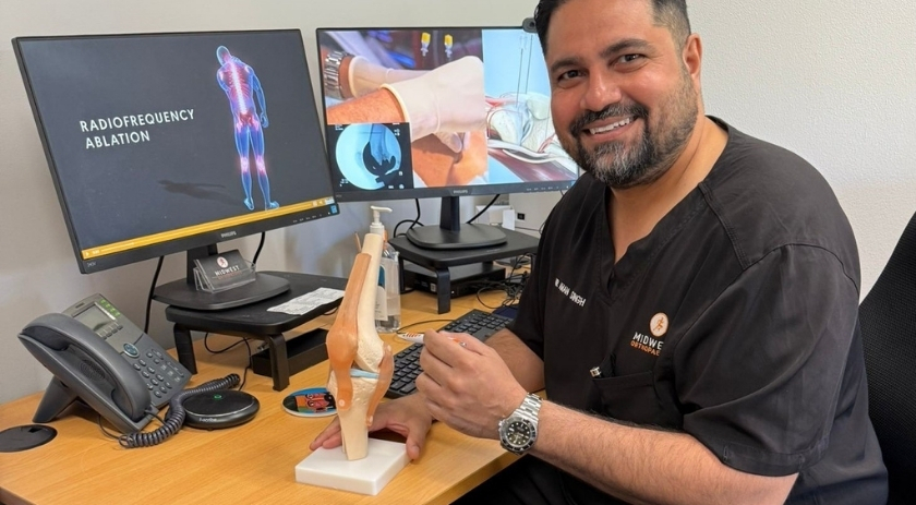 A doctor sitting at a desk, posing with a knee joint model