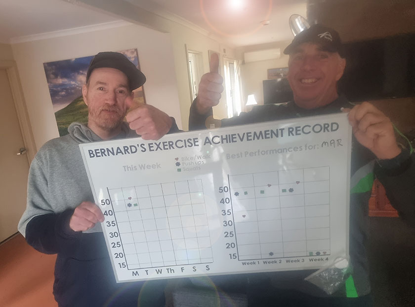 St John of God Accord Disability Services client Bernard holding a whiteboard which records his exercise achievements.